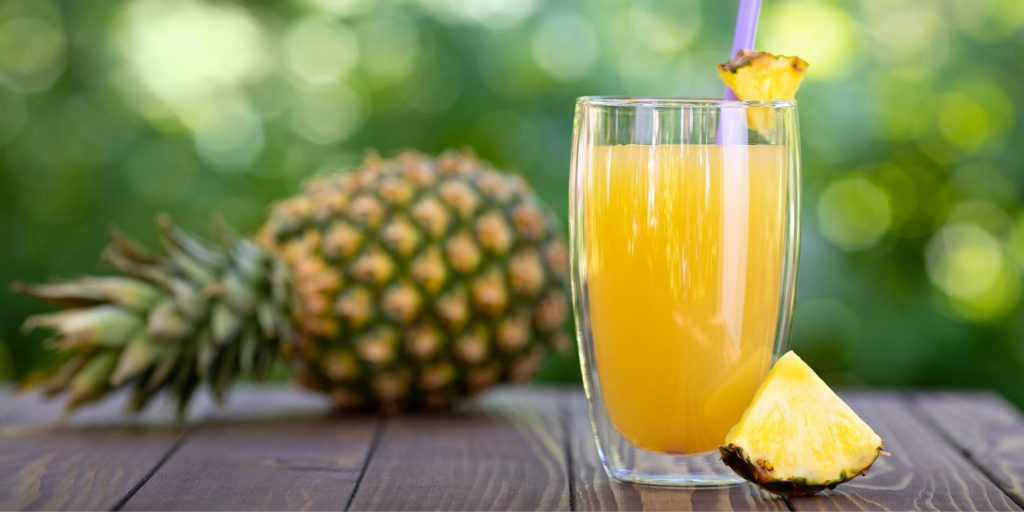 Close up of a glass of fresh pineapple juice on a table outside with a fresh pineapple next to it on a sunny day 