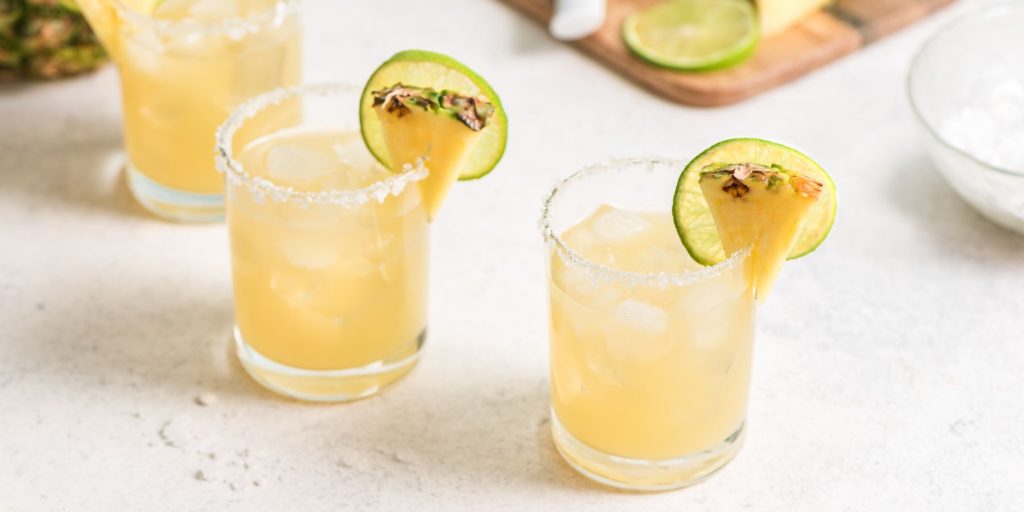 Close up of two Pineapple Paloma cocktails on a white tablecloth in a sunny indoor environment