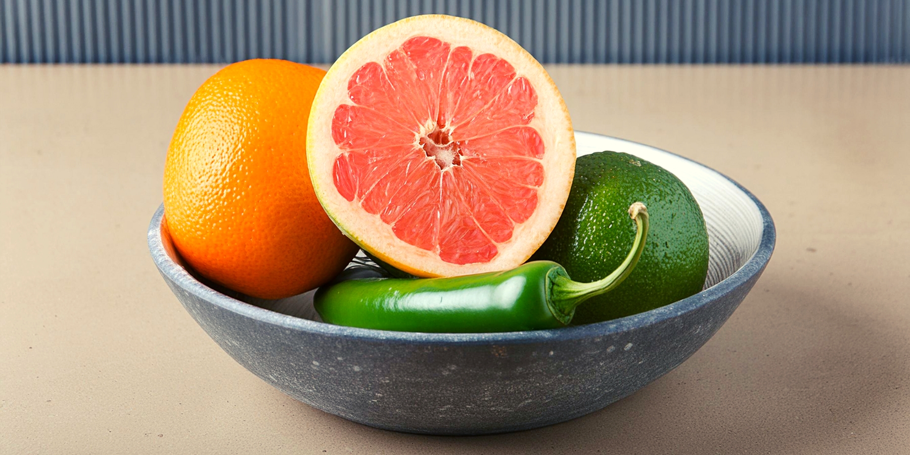 A bowl with a halved grapefruit, an orange, a lime and a jalapeño pepper