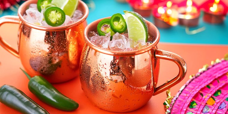 Two Spicy Mexican Mule cocktails served in copper mugs and garnished with sliced jalapeños and lime wedges