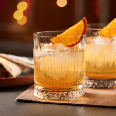 Two Montelobos Mezcal Old Fashioned cocktails with orange wedge garnish served with a burrito