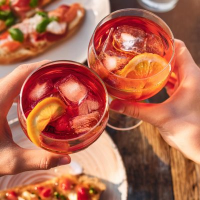 Overhead shot of two hands clinking together two Campari Spritz cocktails