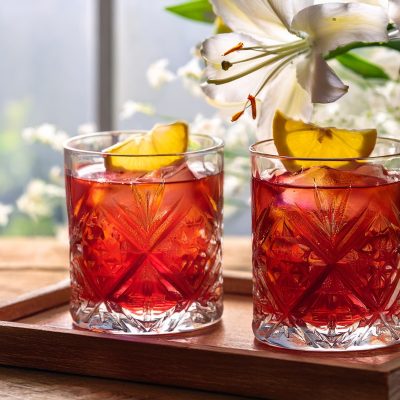 Two Dear Jane cocktails served by a window with a vase of white lilies in the background