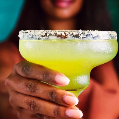 Close-up of a woman's hand holding a Margarita with salted rim to camera