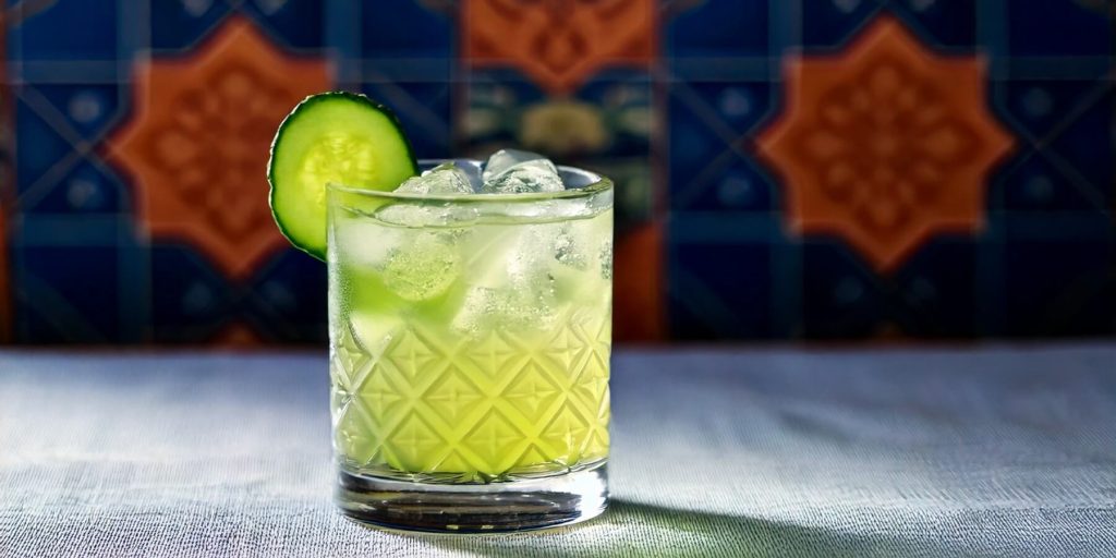 Close-up of a Cucumber Agave Cooler in a rocks glass with ice and sliced cucumber garnish