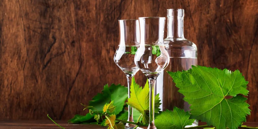 Two pisco brandy glasses with a clear bottle and grapevine leaves, photo by 5ph/Adobe Stock