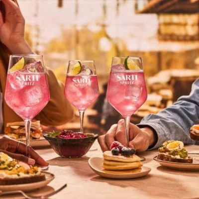 Three friends around a table enjoying Sarti Spritz cocktails alongisde aperitivo bites in the golden light of the late afternoon.
