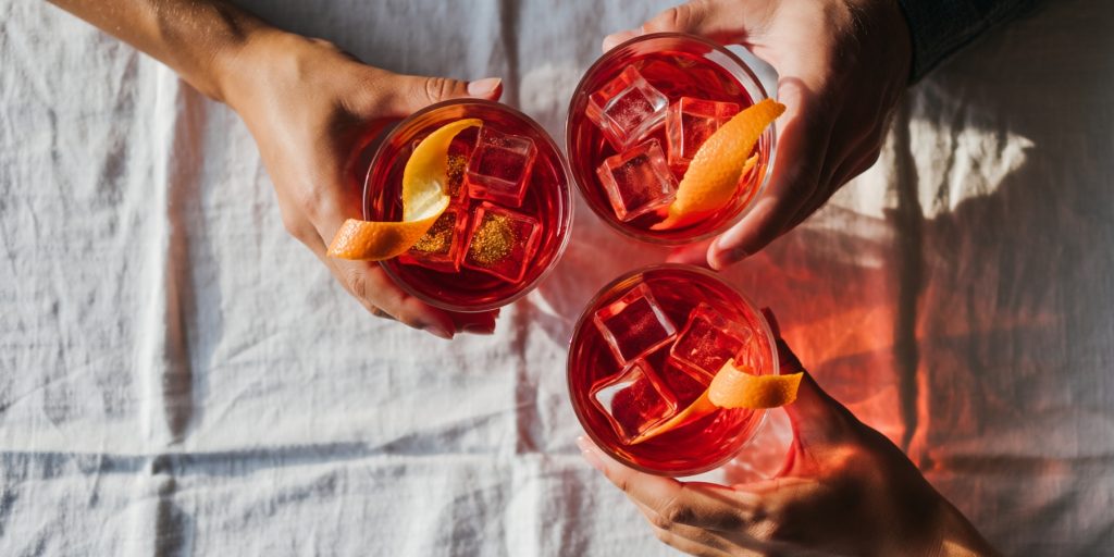 Clinking together 3 glasses of Campari with ice over a table with a white tablecloth