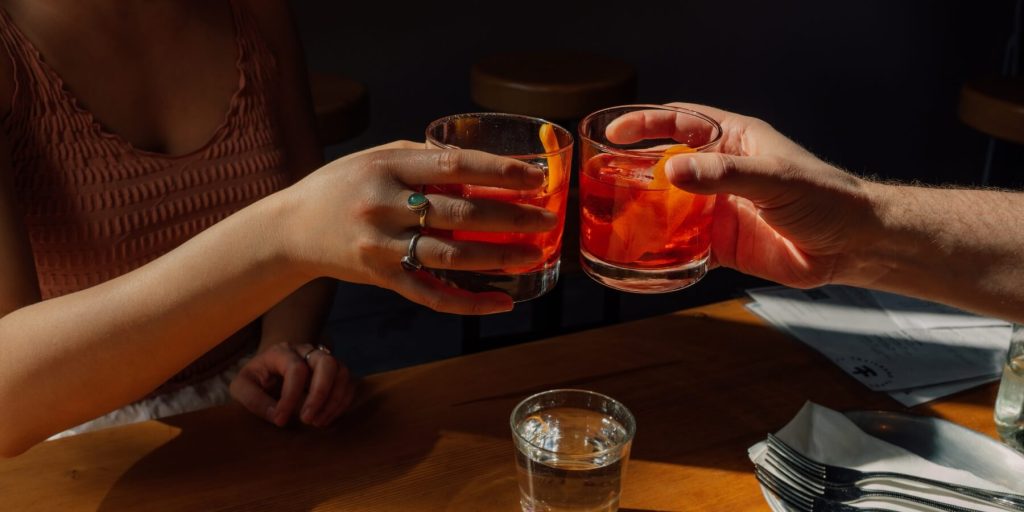A close up of two friends toasting with two Negroni cocktails