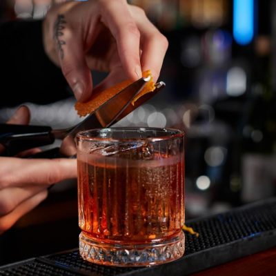 A bartender cutting a slice of orange peel over a Negroni with a pair of scissors