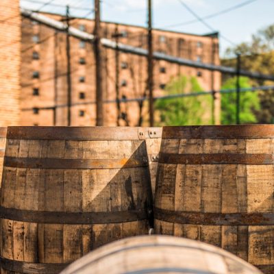 A row of bourbon barrels in front of a face brick distillery.