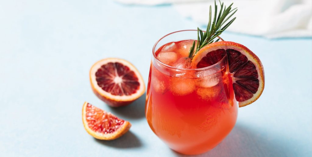 A blood orange Aperol spritz cocktail on a blue and white surface.