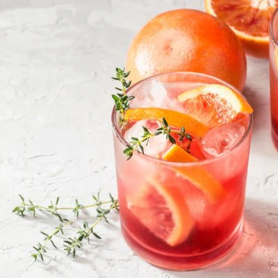 Two blood orange Aperol spritz cocktails garnished with fresh slices of orange and thyme.