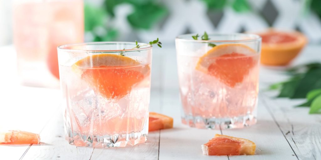 Two grapefruit and fresh thyme spritz cocktails on a white wooden surface.