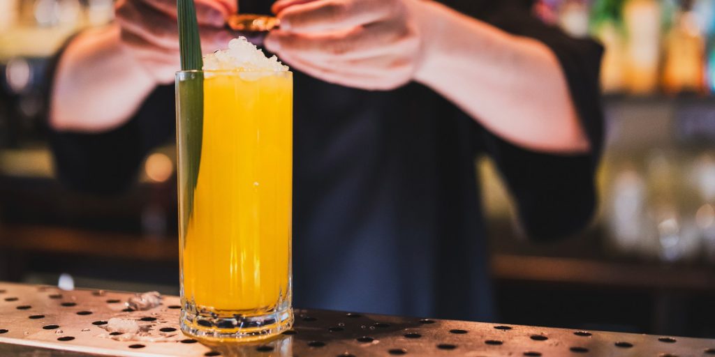 A bartender garnishing a bright yellow passion fruit cocktail on a bar counter.