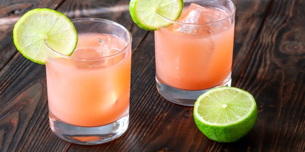 Two guava margarita cocktails garnished with lime wheels on a wooden surface.