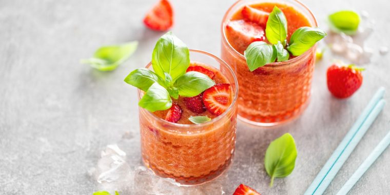 Top view of two Strawberry Basil Cocktails garnished with fresh basil, presented on a light grey surface