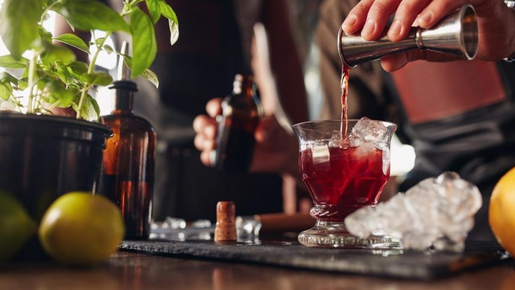 Hand pouring cocktail over ice in tumbler glass