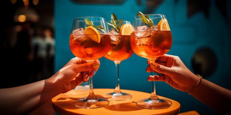 Two hands removing Aperol Spritz cocktails off a table during aperitivo hour