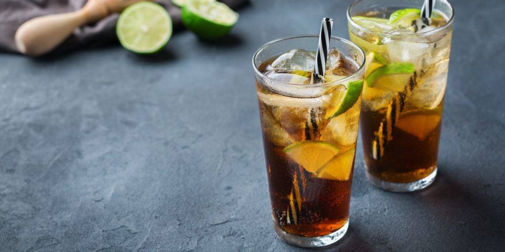 Long island iced tea alcohol cocktail drink beverage, long drink in a glass with straw, ice and lime on a dark table.