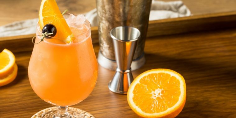 Hurricane Cocktail on a wooden board garnished with orange wedge and maraschino cherry