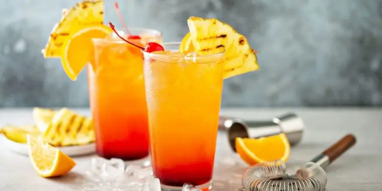 2 tall glasses of Italian Sunrise cocktails garnished with pineapple