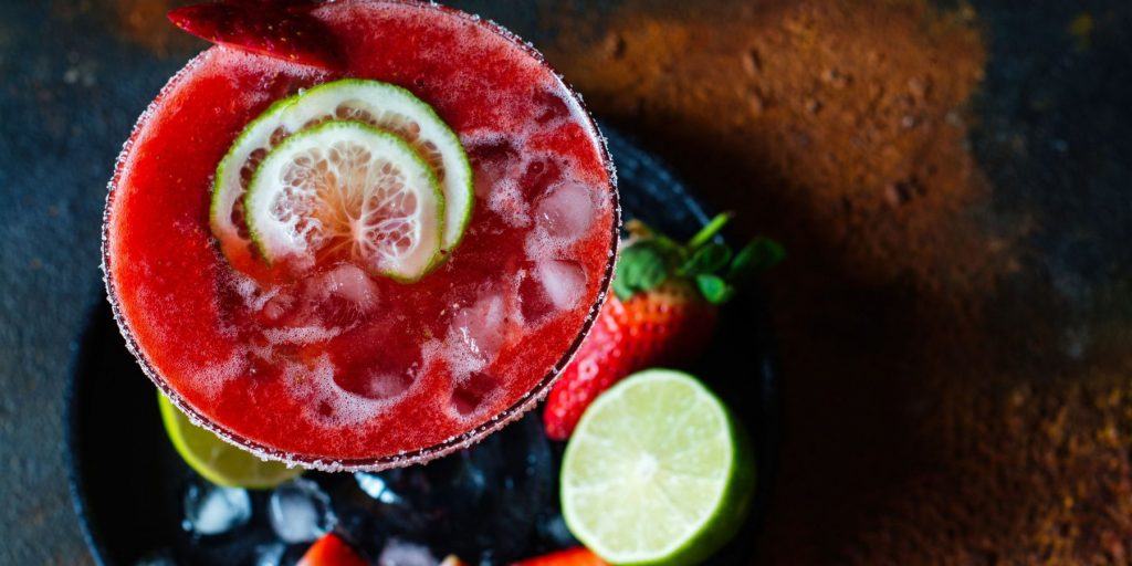 Overhead shot of a strawberry margarita with slices of lime on a wooden surface