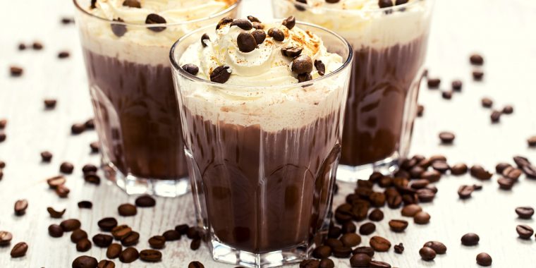 Close-up of a trio of decadent Mexican Coffee Cocktails with whipped cream topping, garnished with coffee beans, posed on a white surface scattered with coffee beans