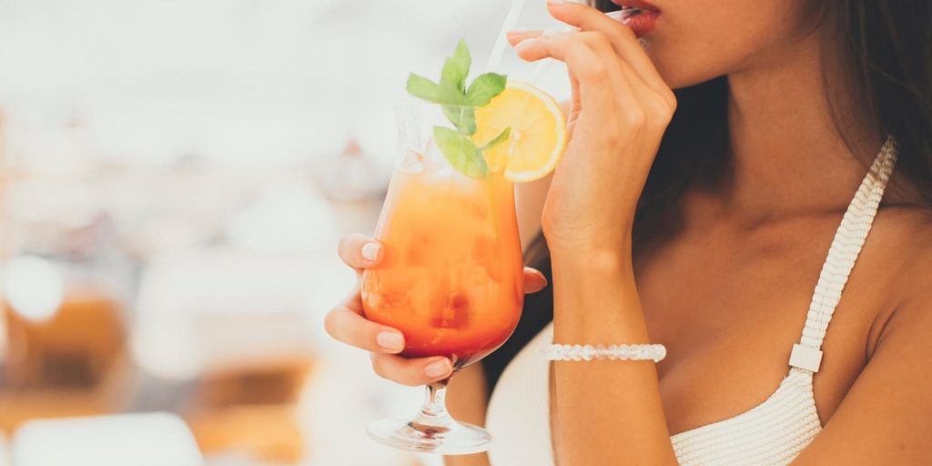 Side-view of a woman sipping an orange colored mocktail through a straw