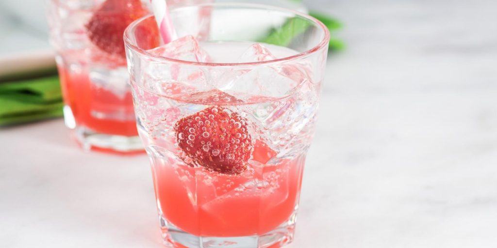 Close up of a Shirley Temple mocktail in a tumbler with ice and fresh strawberry