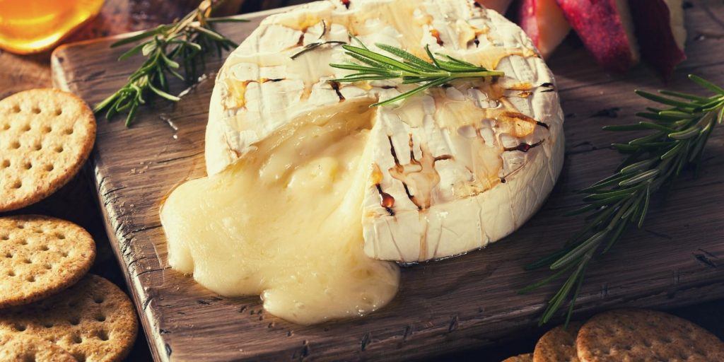 Delicious melting baked brie with crackers on wooden platter