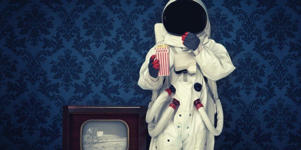 Person dressed in space suit next to a vintage television broadcasting the moon landing