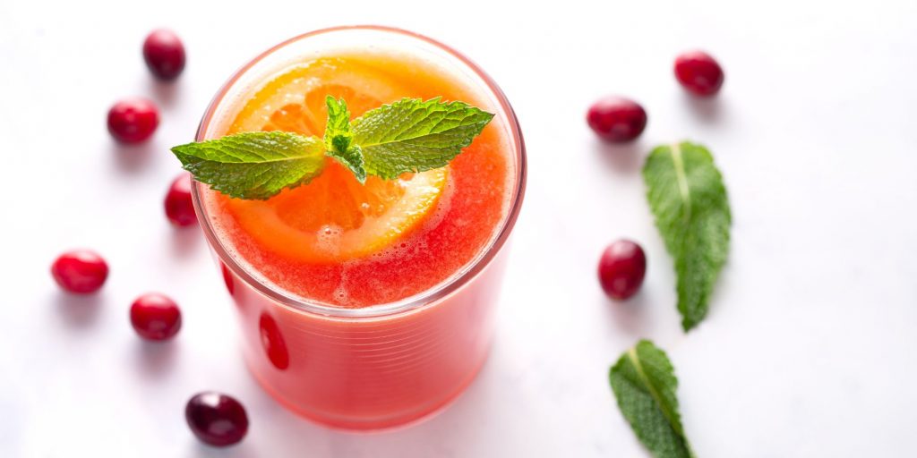 Close up top view of a Madras cocktail garnished with a fresh slice of orange and some mint surrounded by fresh cranberries