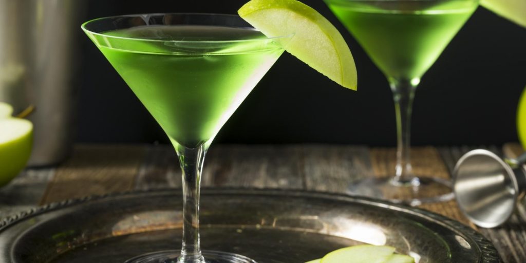 Close up of two bright green Apple Martinis with sliced apple garnish, presented on a small silver tray, set on a rustic wooden surface