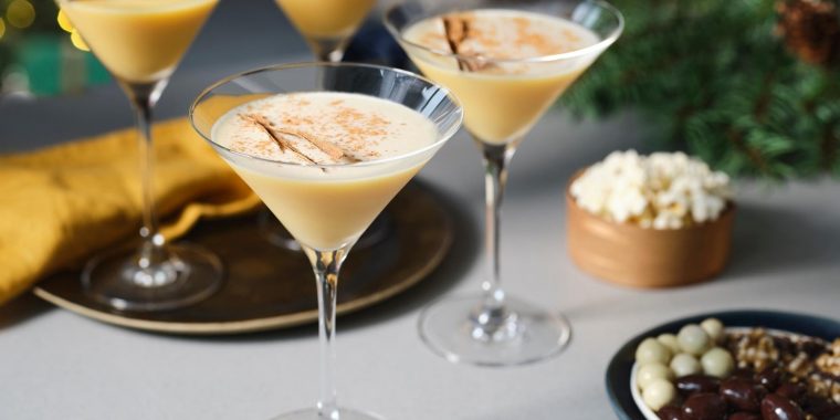 A trio of indulgent Eggnog Martini cocktails presented in long-stemmed Martini glasses, surrounded by snack bowls on a light grey surface