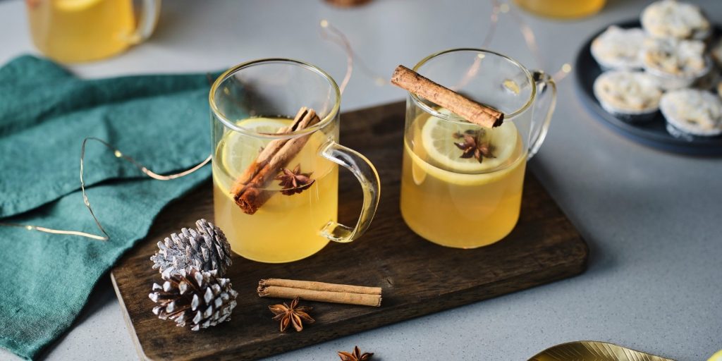 Two Hot Toddy Cocktails garnished with whole sticks of cinnamon and star anise., presented on a wooden platter among Christmas trimmings