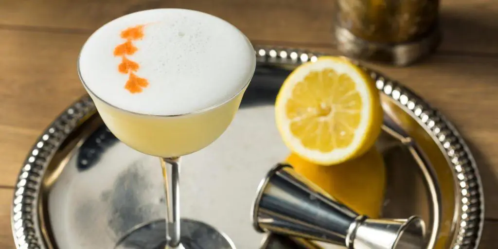 Top view of traditional Whiskey Sour topped with egg white foam and drops of orange bitters