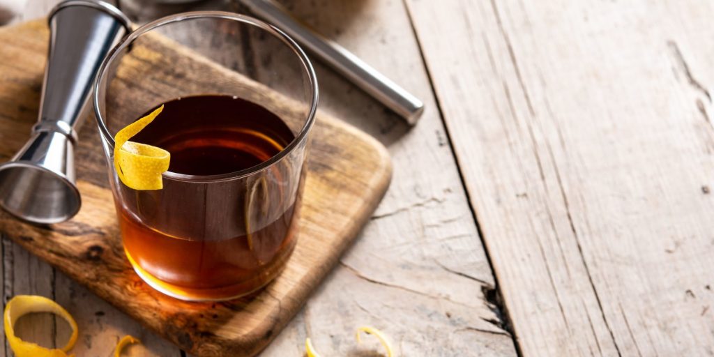 Close up top view of a Sazerac cocktail on a wooden platter, on a wooden table, with lots of natural light streaming in from the window behind. 