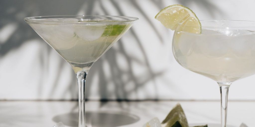Close up of two Frozen Margaritas in a coupe and Martini glass respectively, posed against a white wall with palm leave shadows in the background