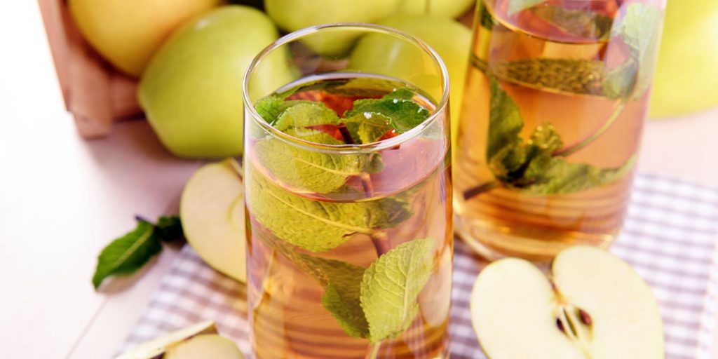 Two glasses of Apple Cider Long Island Iced Tea on a table with a gingham table cloth surrounded by fresh, cut apples