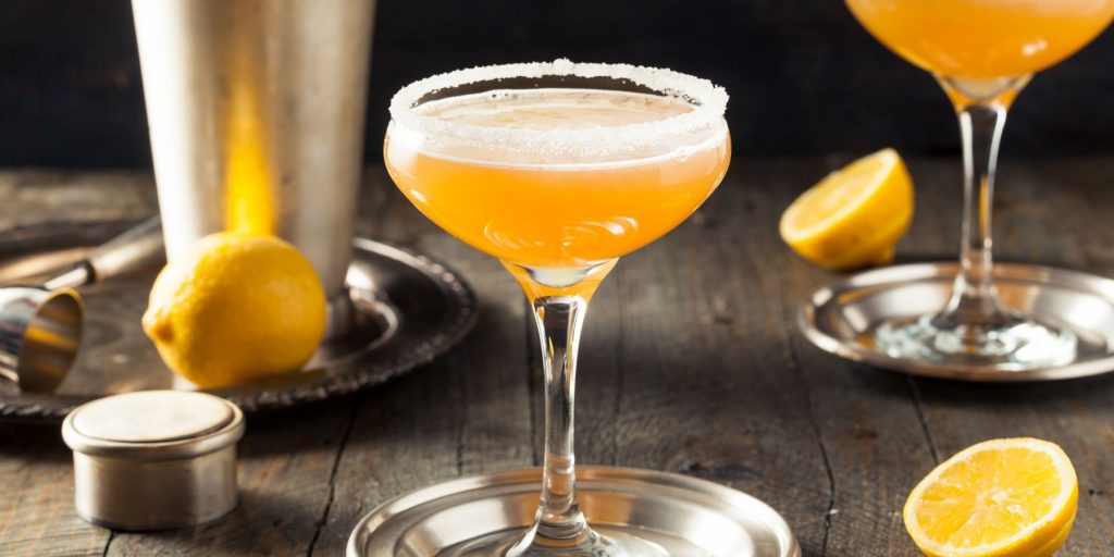 A pair of sugar-rimmed Vodka Side Car cocktails served on silver serving dishes on a wooden surface