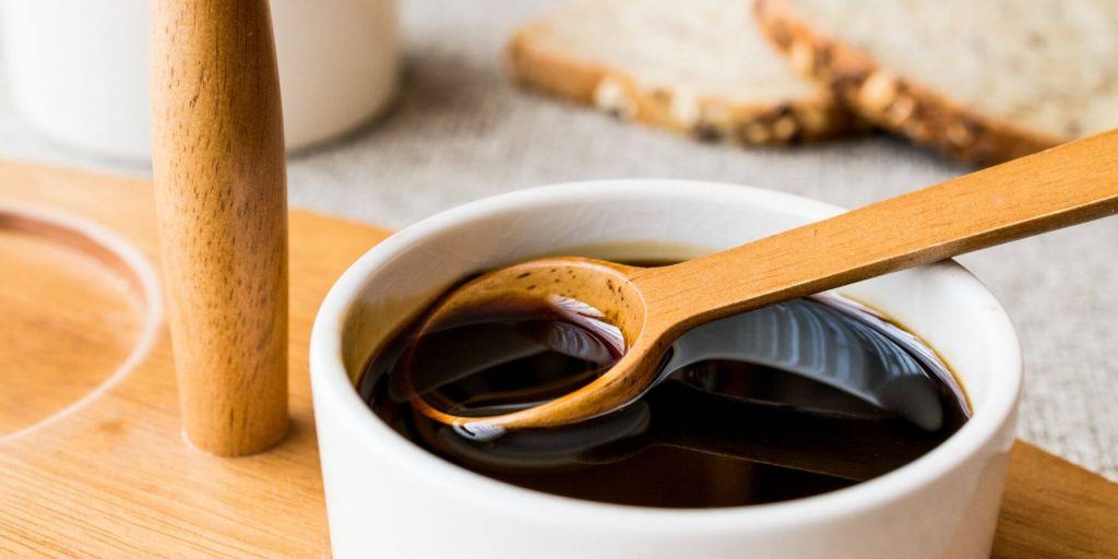 Molasses syrup in a small white bowl with wooden spoon