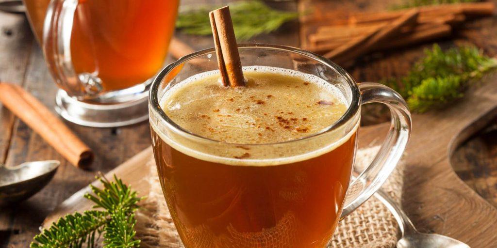 Two Hot Buttered Rum cocktails in mugs, garnished with a cinnamon stick each