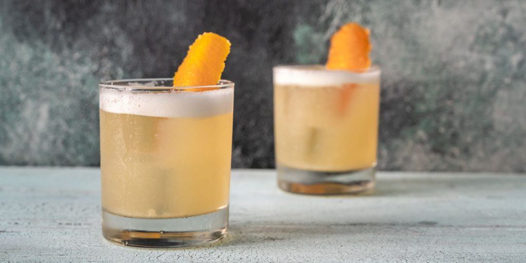 A pair of Whiskey Sour Cocktails posed against a grey marble finish backdrop