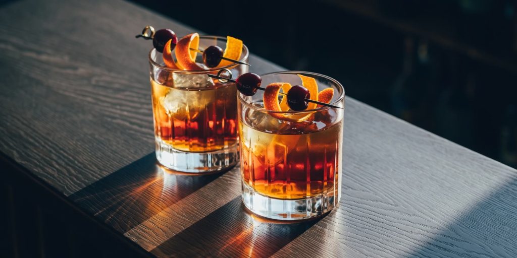 Two Maple Old Fashioned cocktails in elegant rocks glassed, garnished with orange peel and dark cherries 