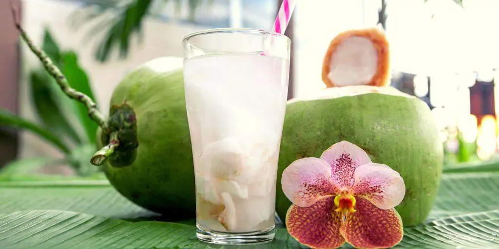 Coconut water cocktail with fresh coconuts in the background
