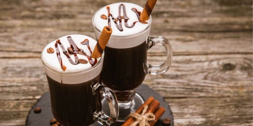 Two Irish Coffee glasses garnished with chocolate drizzle presented on a wooden table