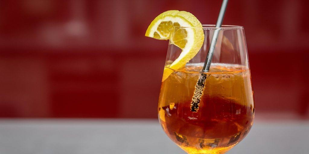 A stemless glass of Apple Cider Spritz garnished with a a slice of lemon featured against a red backdrop