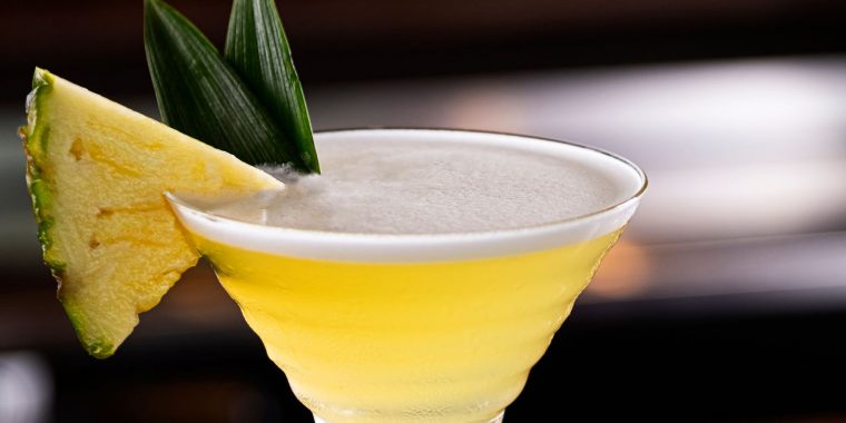 Extreme close up of a Pineapple Martini garnished with a fresh slice of pineapple, presented against a dark backdrop