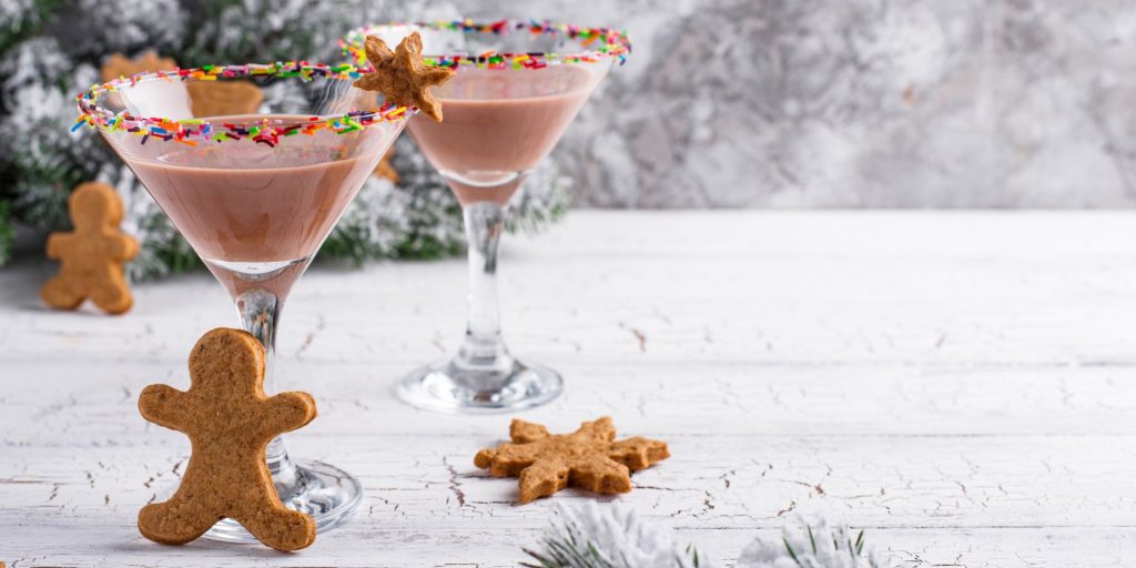 Two Gingerbread Martini cocktails on a white table in a home lounge decorated for the holidays, with freshly baked gingermen biscuits around it